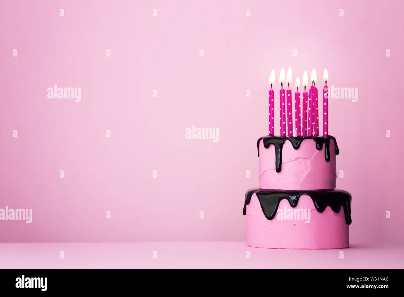Pink tiered birthday cake with drip icing and lots of candles Stock ...