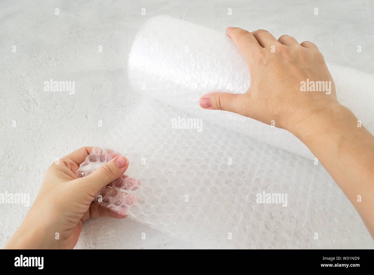 Woman hands holdind a roll of white transparent bubble wrap on a rough white background