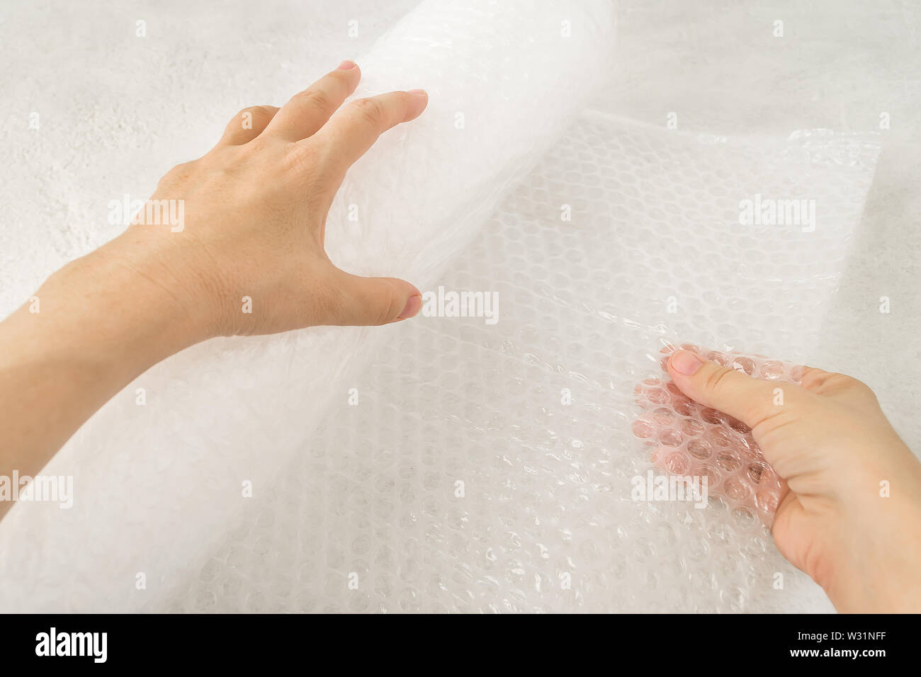 Woman hands hold a roll of white transparent bubble wrap on a rough