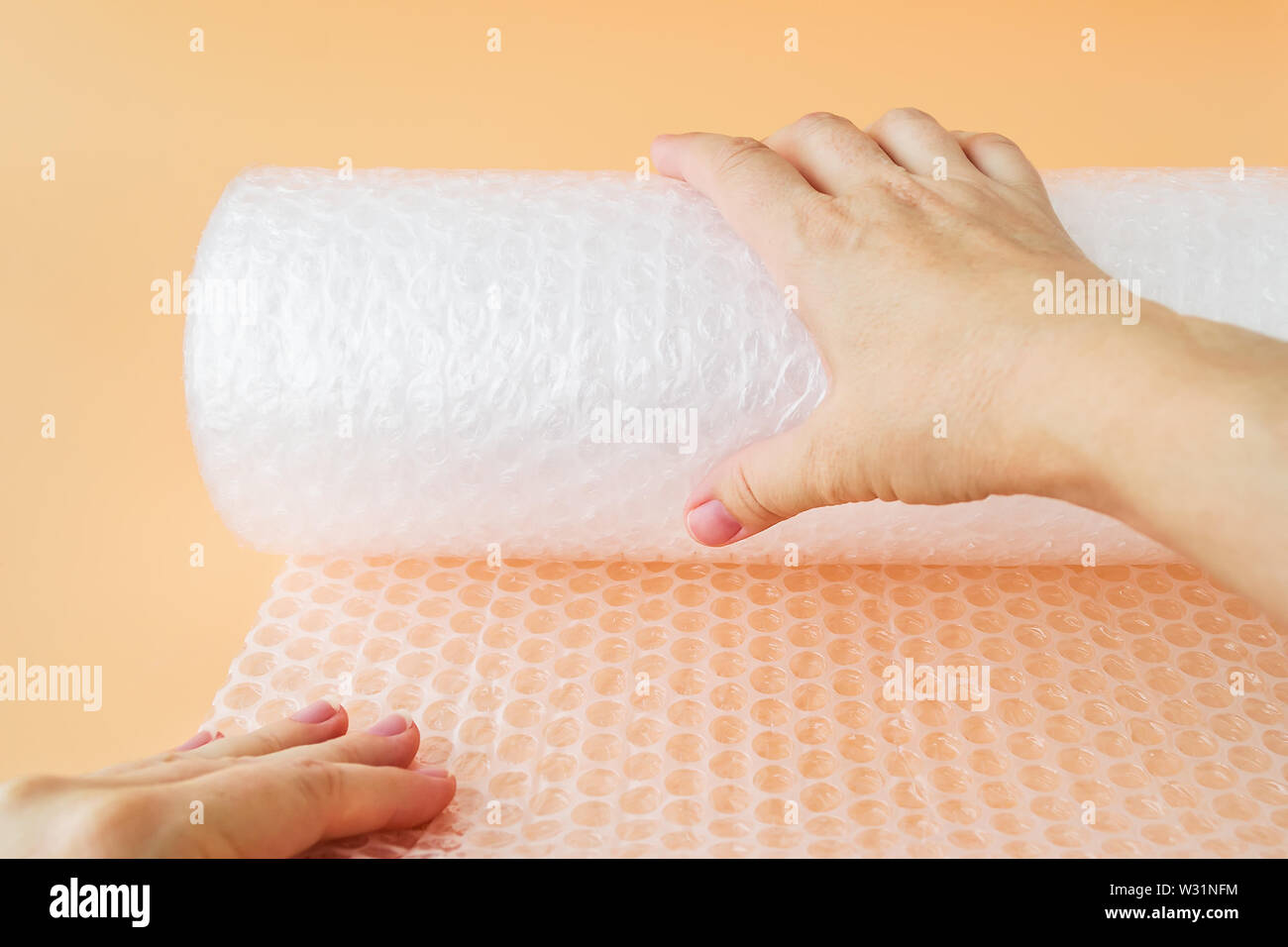 Woman hands unwind a roll of white transparent bubble wrap on a yellow background. Material for