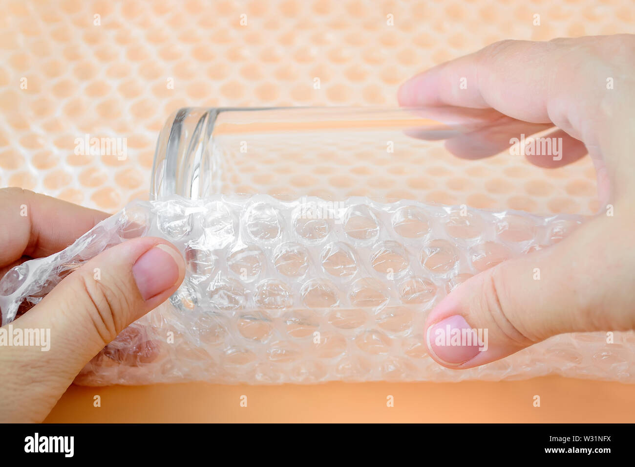 Woman hands package glass for water with transparent bubble wrap on a yellow background