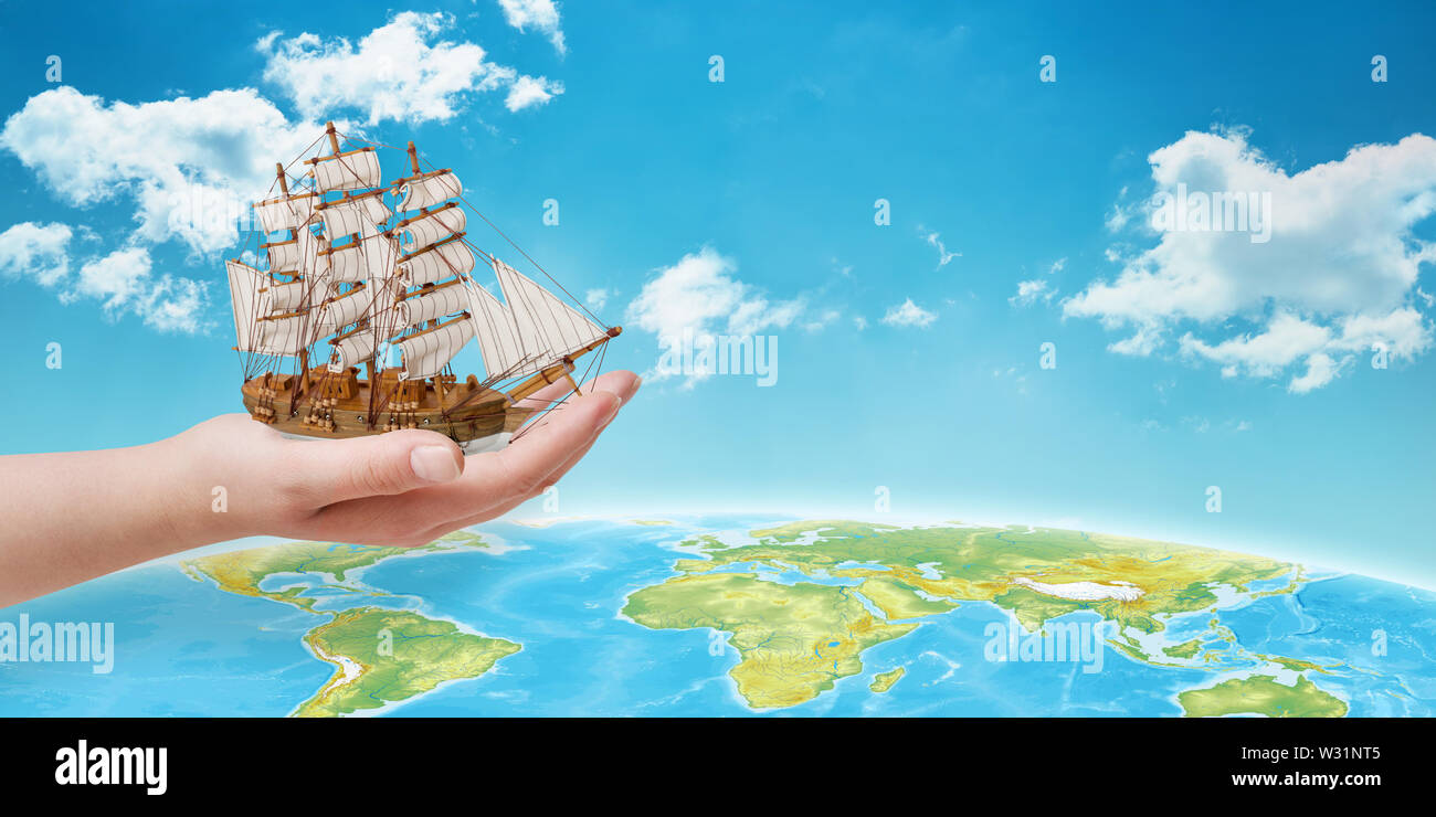 Hand holding the ship over the globe. Concept of traveling across the sea. Free space beside fot text. Stock Photo