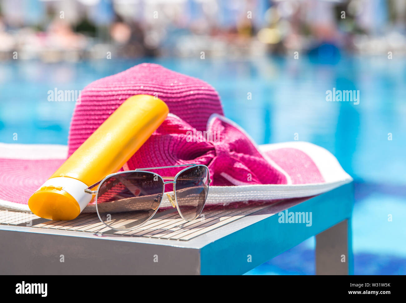 Bottle of sunscreen, hat and sunglasses next to swimming pool in hotel with  palms on background Stock Photo - Alamy