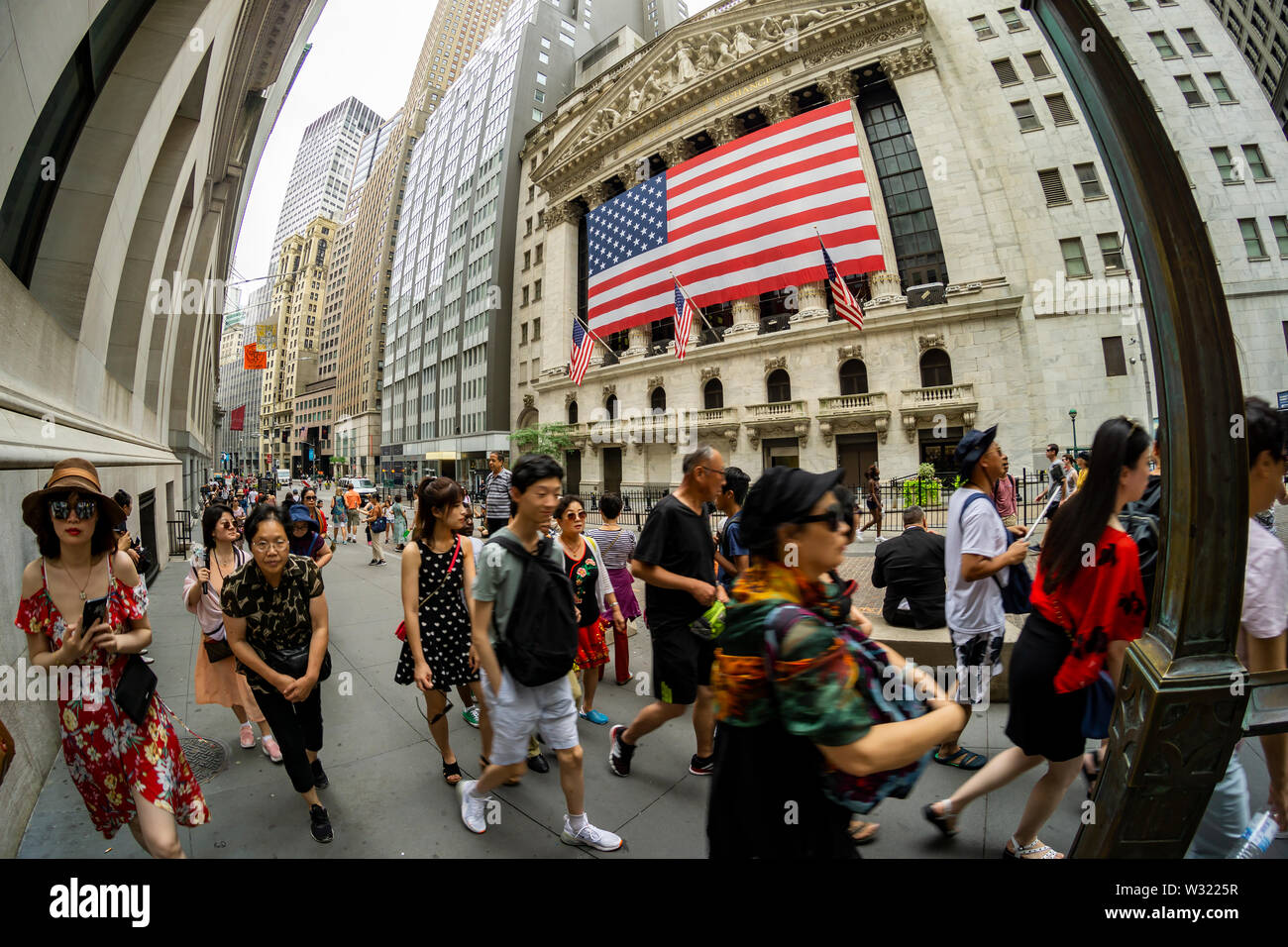 Hordes of Asian tourists pass the New York Stock Exchange, decorated with a giant American Flag for Independence Day, on Wednesday, July 3, 2019. The stock exchange has a short trading day, closing at 1:00PM today, prior to the July 4th holiday. (© Richard B. Levine) Stock Photo