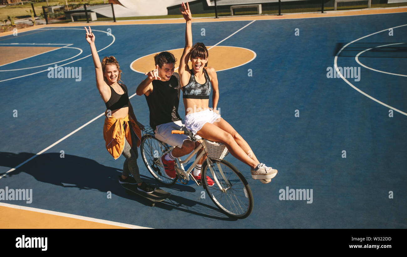 Group of three friends with skateboard and bicycle on basketball court outdoors. Friends hanging out outdoors. Stock Photo
