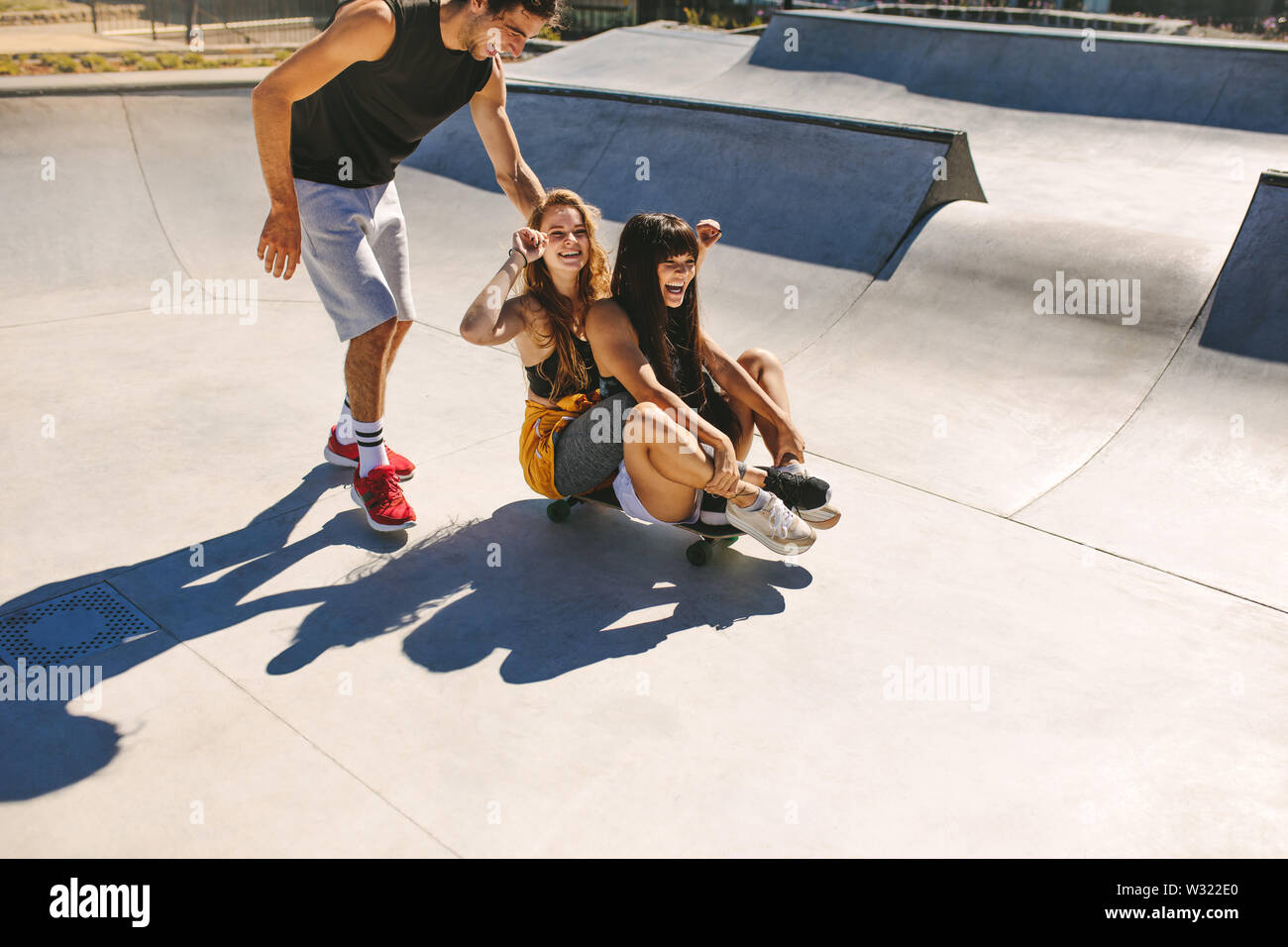 Group of friends having fun at skate park. Young man and two girls playing with a skateboard at skate park. Stock Photo