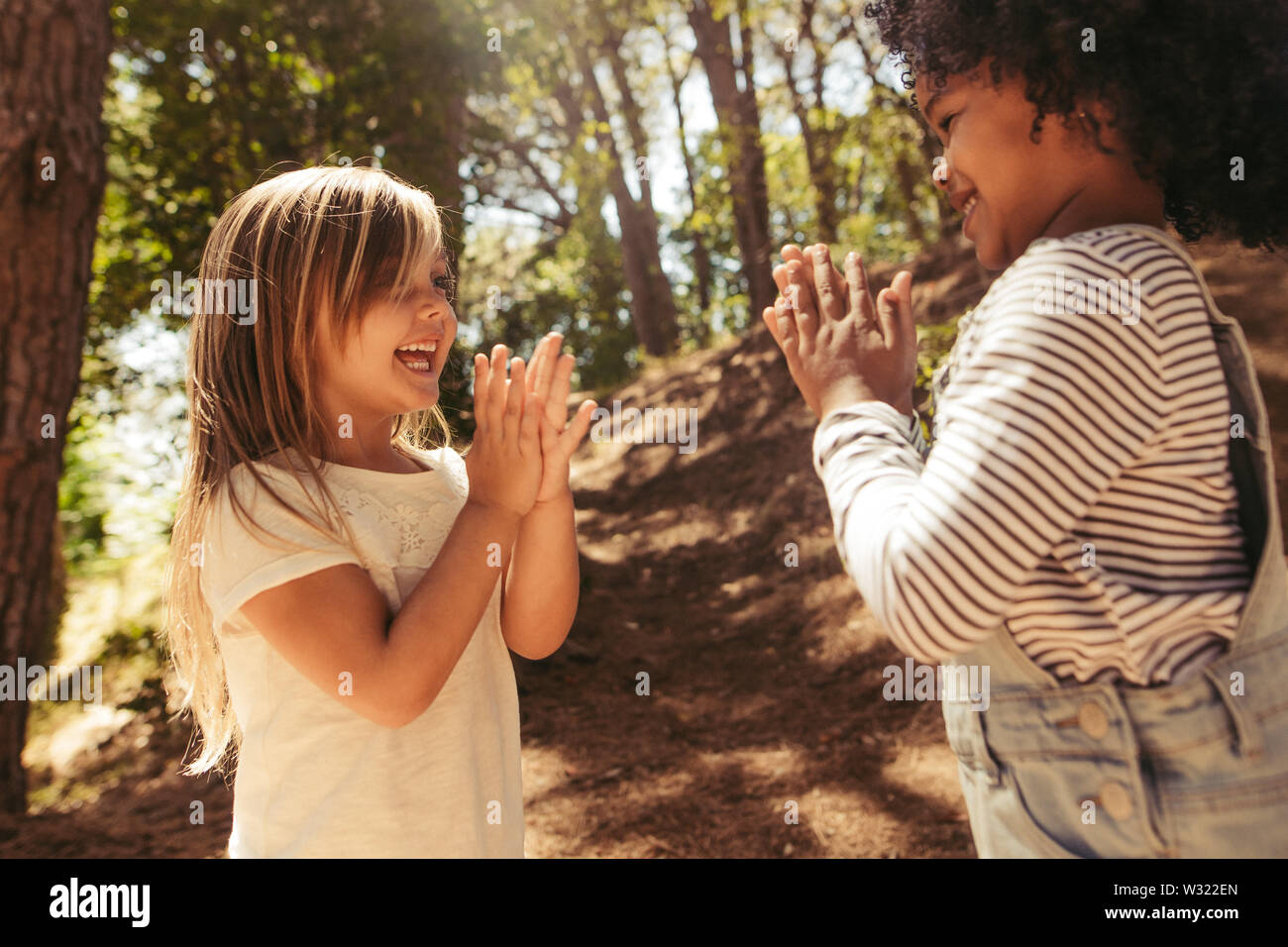 Cute girls playing clapping games outdoors. Children playing games in forest. Stock Photo