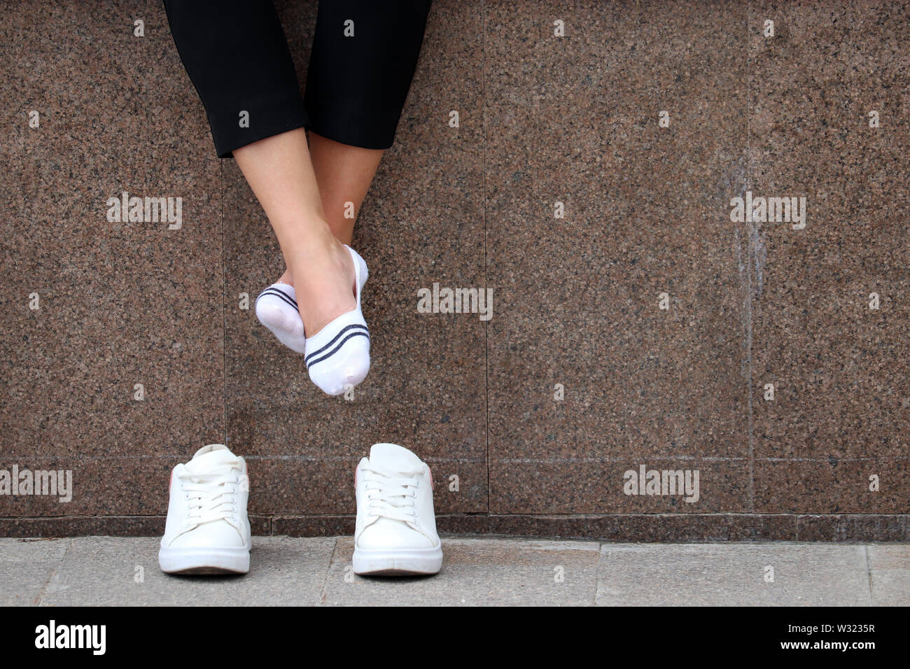 Tired legs, barefoot woman with removed white sneakers resting on a street. Female feet in white socks, girl sitting and relaxing after running Stock Photo