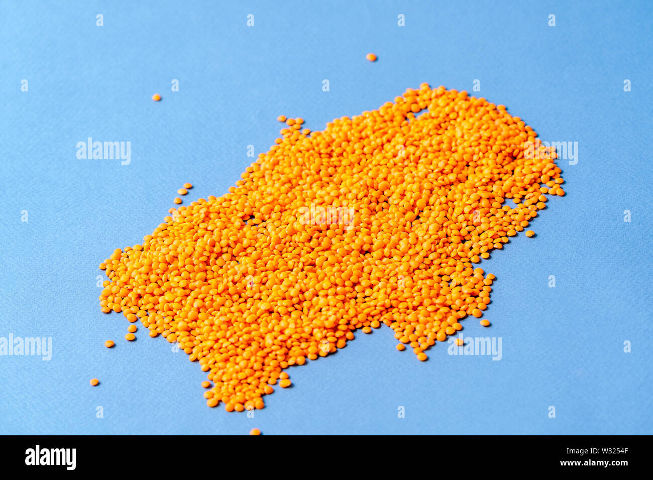 Pattern with Small orange lentils seeds of annual legume plant, over blue background. Stock Photo