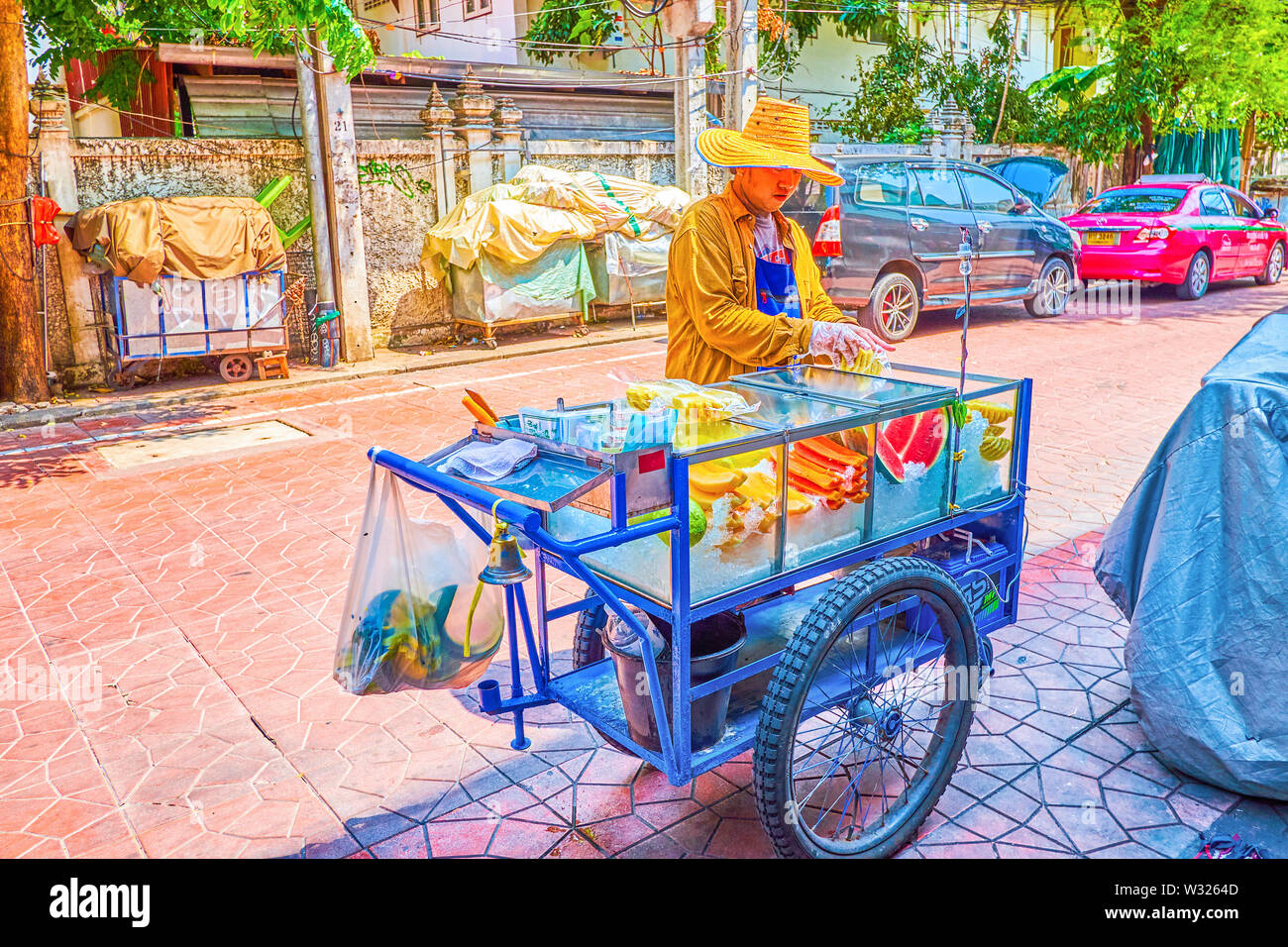 BANGKOK, THAILAND - APRIL 22, 2019: The merchant sells fresh fruits, the heaps of them lie in ice in the glass showcase of his cart, on April 22 in Ba Stock Photo