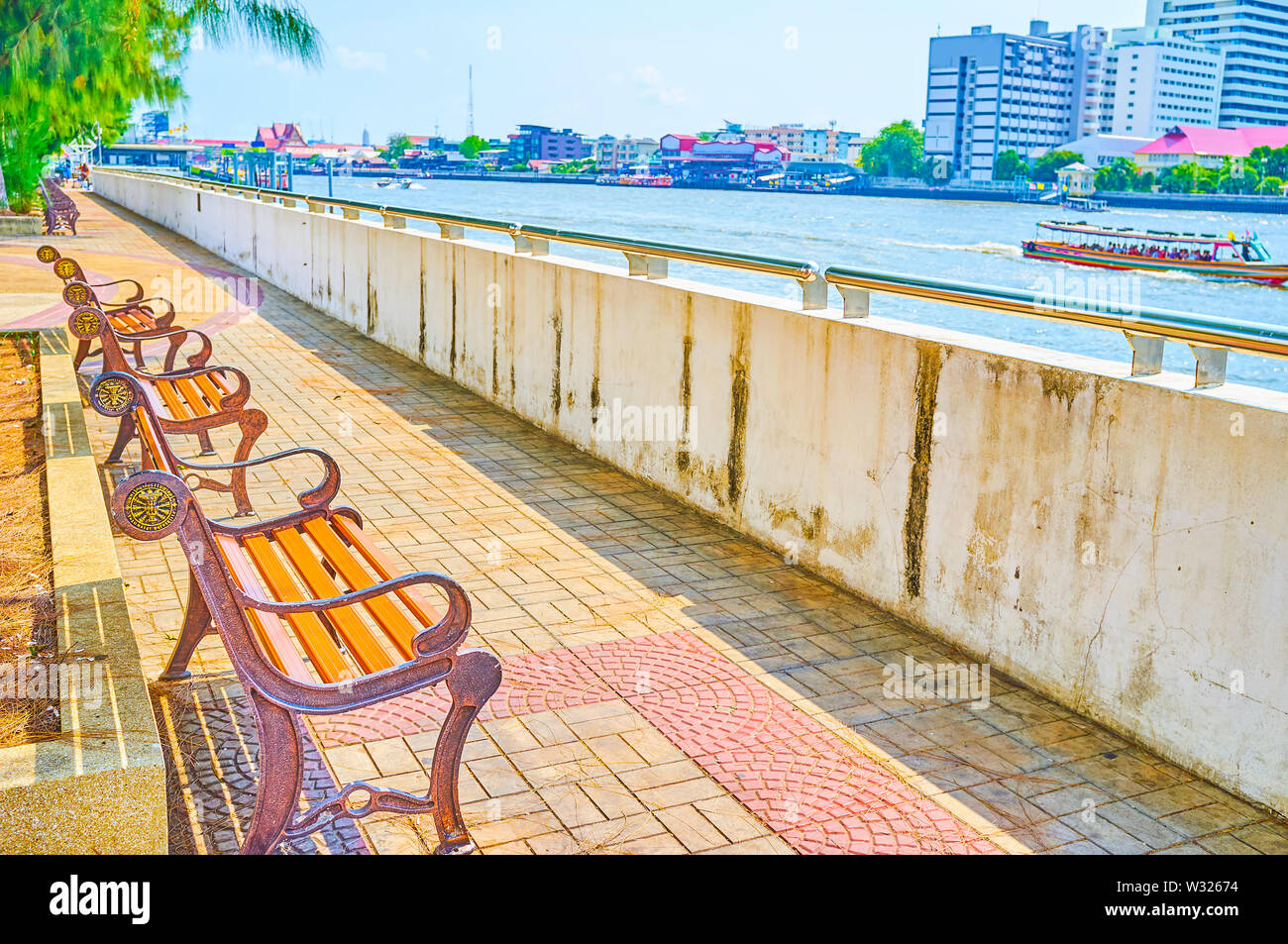 BANGKOK, THAILAND - APRIL 22, 2019: The narrow riverside promenade of Tammasat University with line of benches with a greay view on Chao Phraya river, Stock Photo