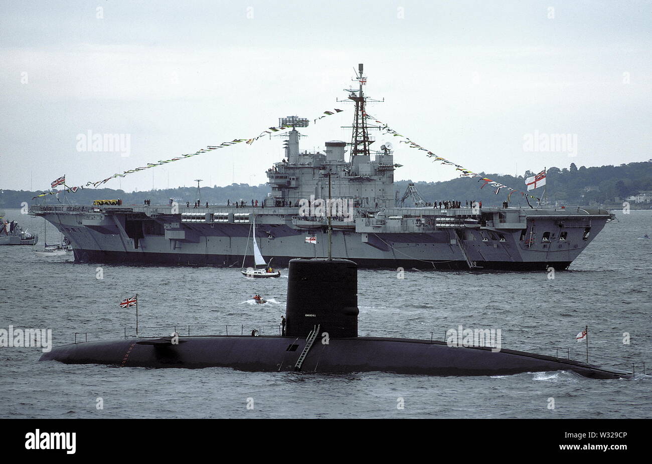 AJAXNETPHOTO. 1977. SPITHEAD, ENGLAND - NUCLEAR POWER - HMS CHURCHILL, 4,900 TONS, COMPLETED IN 1970, WAS ONE OF THE FIRST ALL NUCLEAR POWERED SUBMARINES IN THE BRITISH ROYAL NAVY. SEEN HERE AT THE SILVER JUBILEE FLEET REVIEW; IN THE BACKGROUND IS THE AIRCRAFT CARRIER HMS HERMES.  PHOTO:JONATHAN EASTLANDAJAX.  REF:CD21207 1 91. Stock Photo