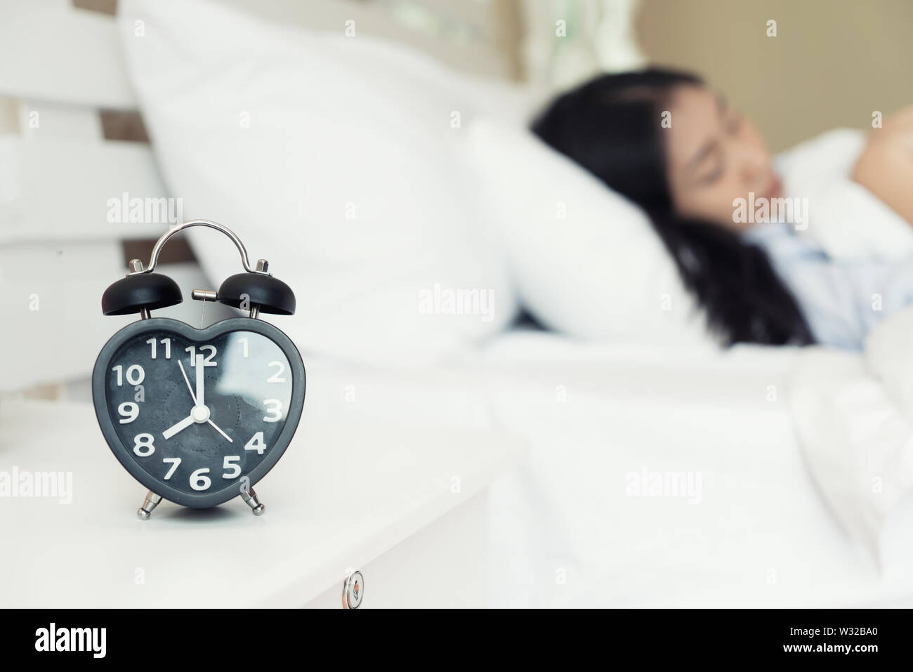 Tired Asian young woman. Wake up in the morning, Defocus woman sleep on bedroom, Alarm with time 8 o clock am, sleepy and lazy dont want getting out o Stock Photo