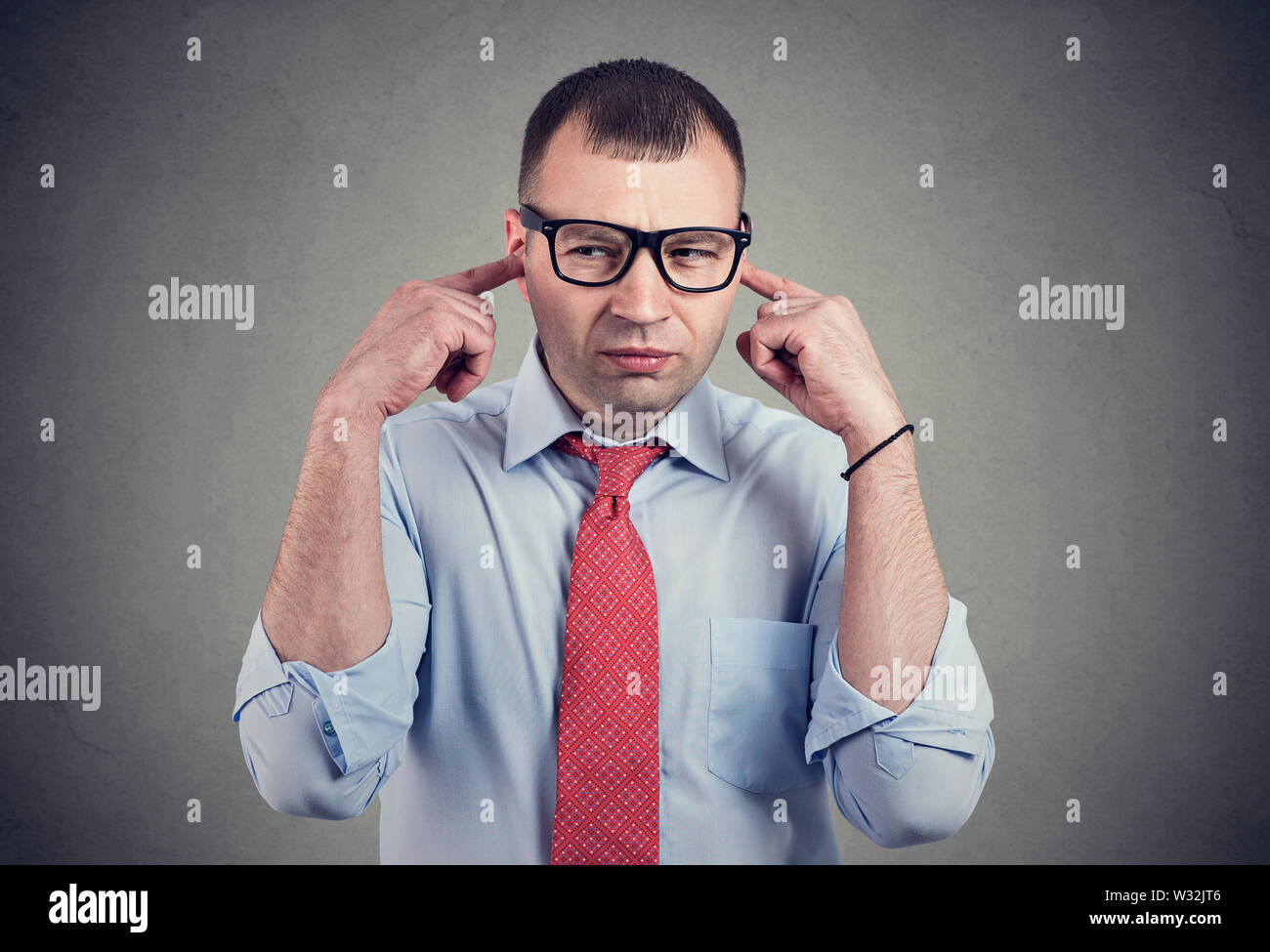 Annoyed man looking grumpy plugging with fingers ears unwilling to listen to anyone. Stock Photo