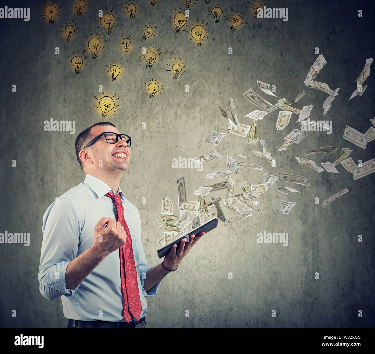 Businessman with bright ideas and tablet building successful online business earning money dollar bills cash falling down. Stock Photo