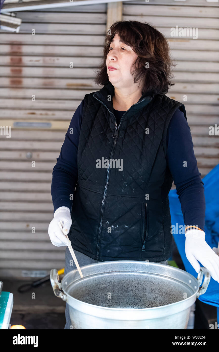 Tokyo, Japan - March 30, 2019: Female street vendor, Japanese woman cooking preparing stock in pot, stirring with chopsticks food in Tsukiji outer out Stock Photo