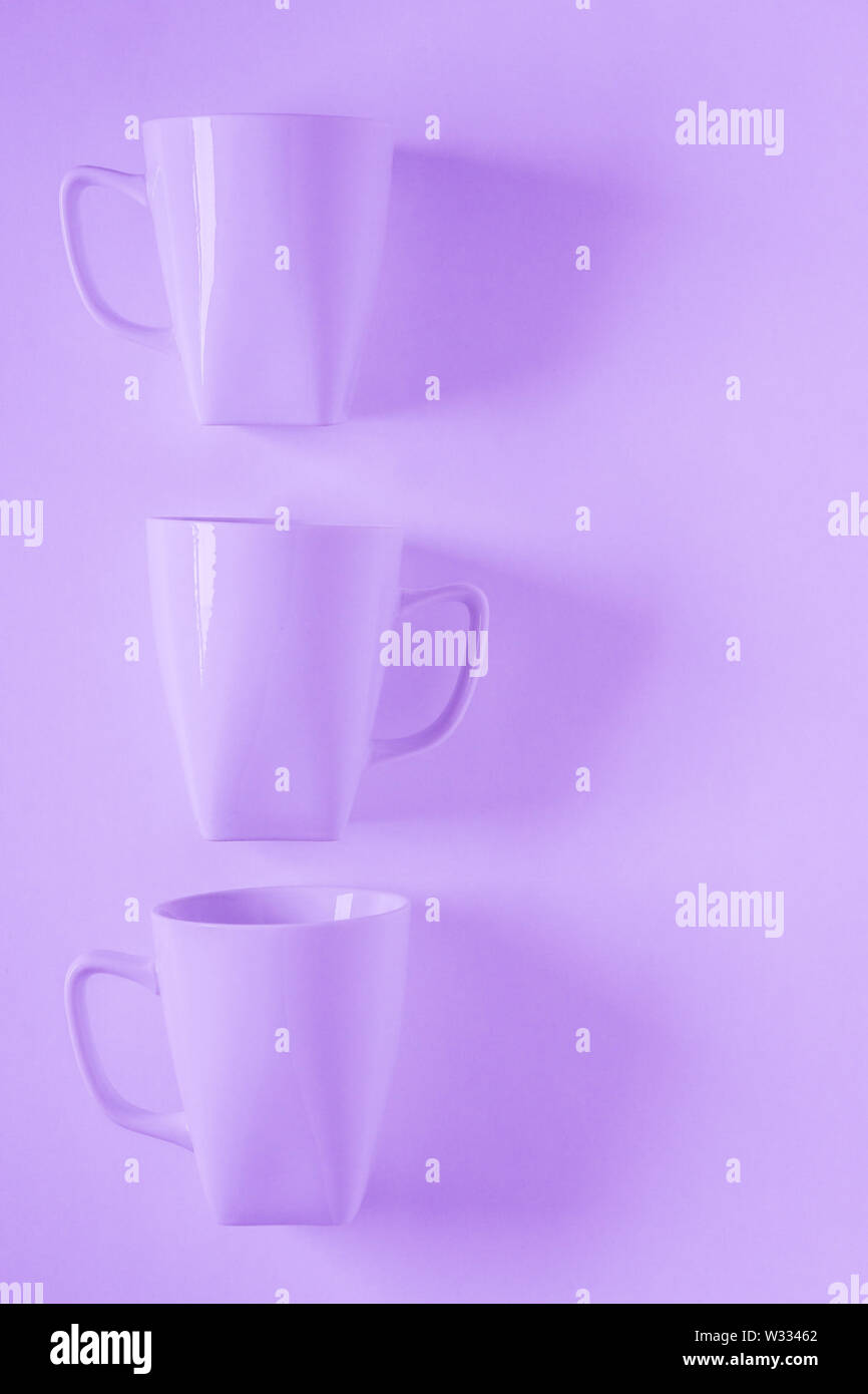 3 monochromatic purple coffee mugs lined up in a row on violet background with blank empty room space for text, copy, or copy space. Modern top view c Stock Photo