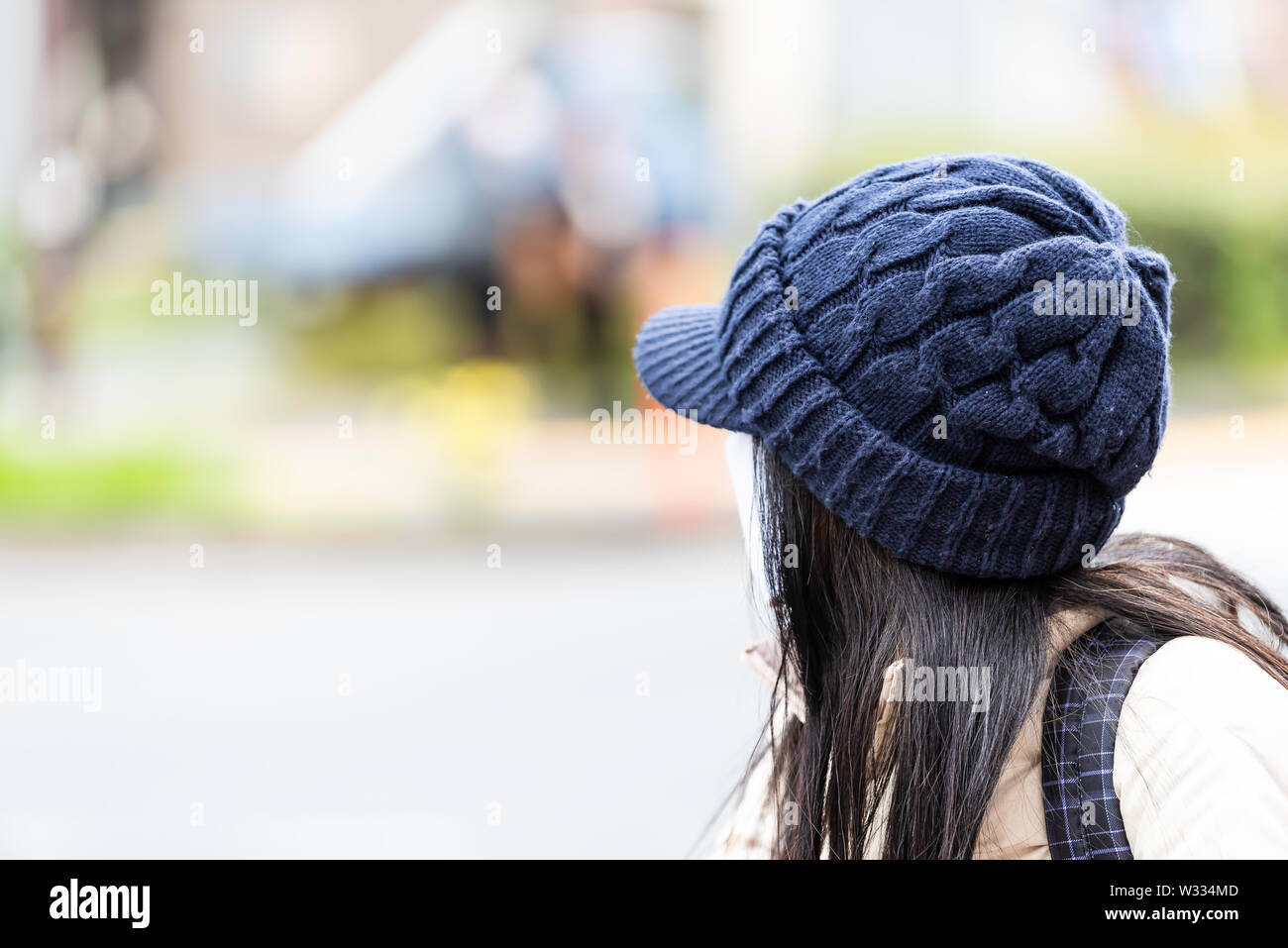 Young Japanese Asian woman standing on street looking back dressed in hat and mask with blurred urban background Stock Photo