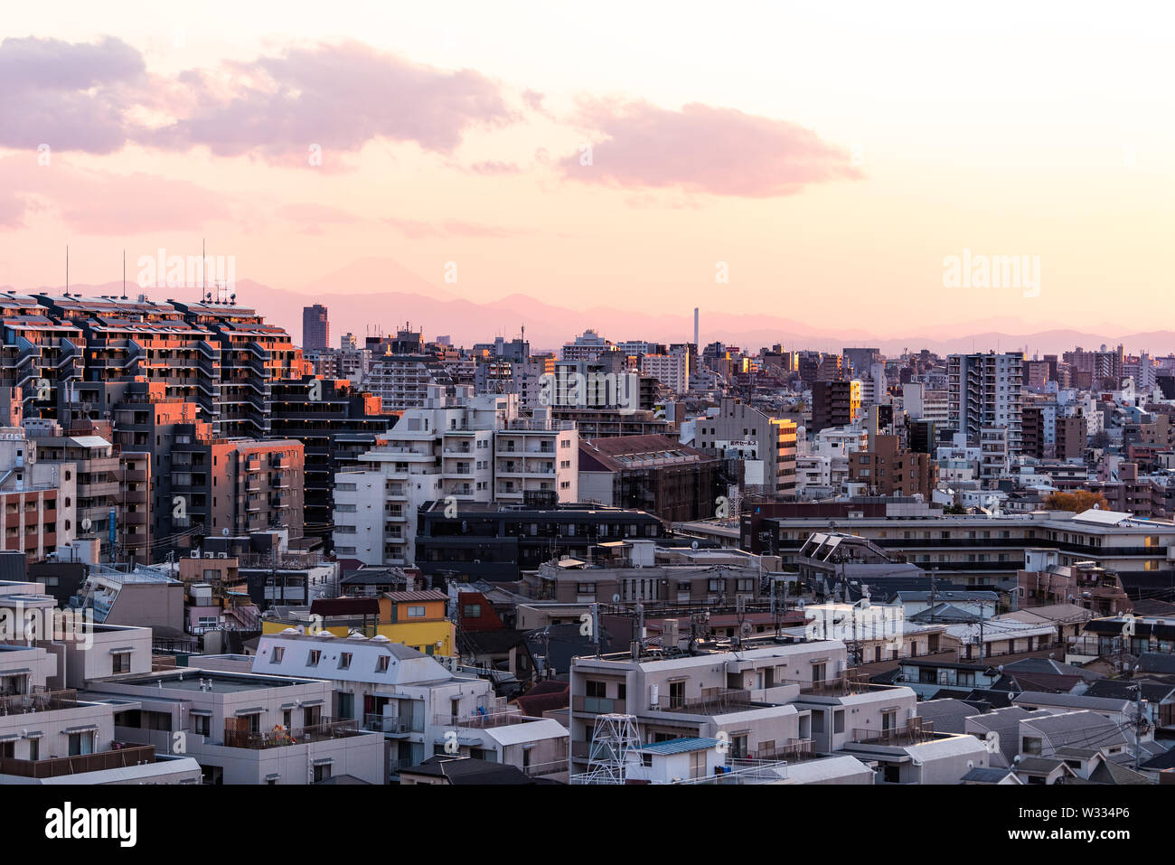 Shinjuku cityscape in Tokyo, Japan at sunset with view of Mount Fuji and golden sunlight with apartment buildings and mountains Stock Photo