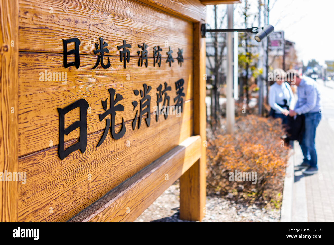 Nikko, Japan - April 4, 2019: Wooden board on street of mountain village with text saying Nikko City Fire Department sign, people in background on sid Stock Photo