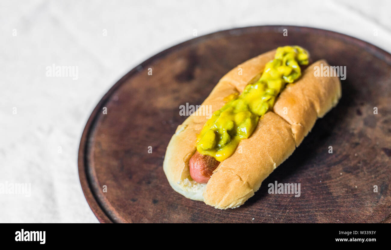 Traditional hot dog with gherkin and mustard relish against white