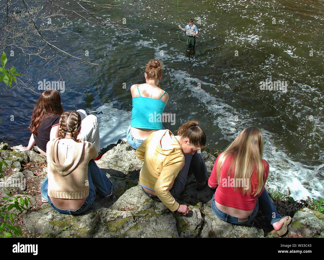 Middlefield, CT USA. May 2016. Young women thinking and sitting on a cliff looking down watching a fisherman in action. Stock Photo