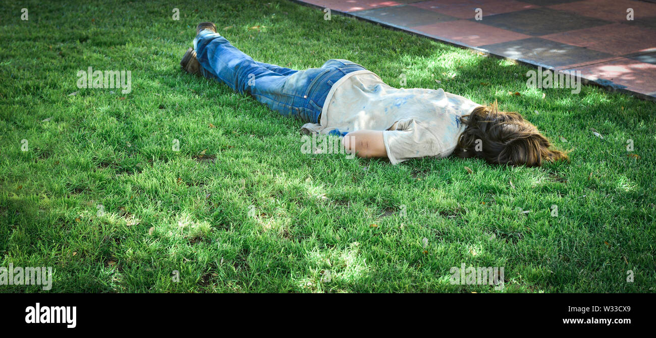 A Caucasion homeless man sleeps face down on the grass in a park in the summertime Stock Photo