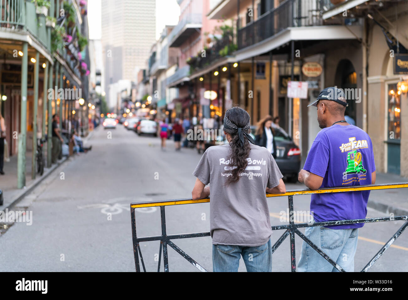 New Orleans, USA - April 22, 2018: Back of two local men standing on Bourbon street road in evening with people walking in blurry background in famous Stock Photo