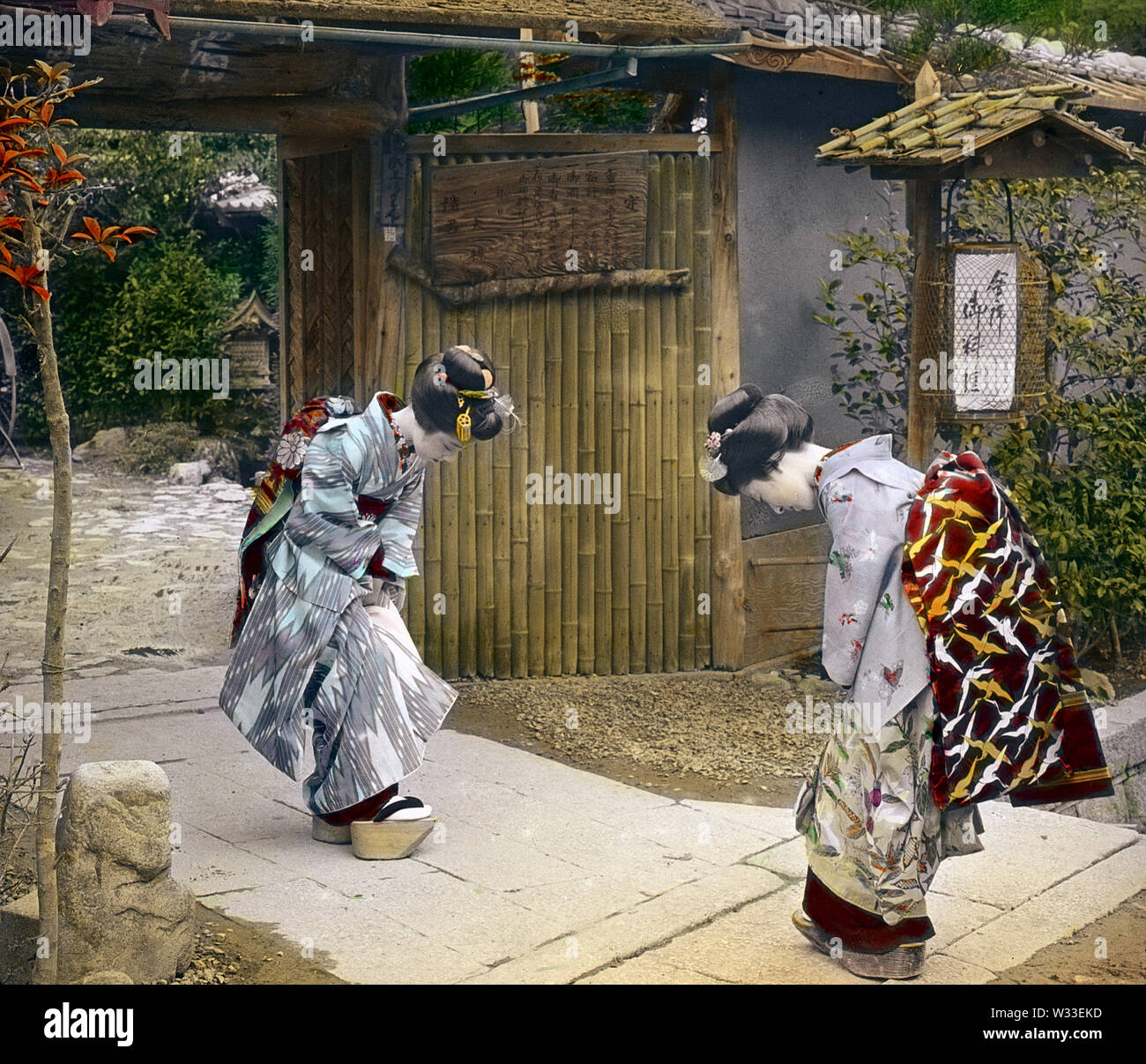 [ 1890s Japan - Japanese Women Greeting ] —   Two women wearing kimono, geta and traditional hairstyles bow to each other at the entrance gate to Genkyu-en Gardens in Hikone, Shiga Prefecture.  19th century vintage glass slide. Stock Photo
