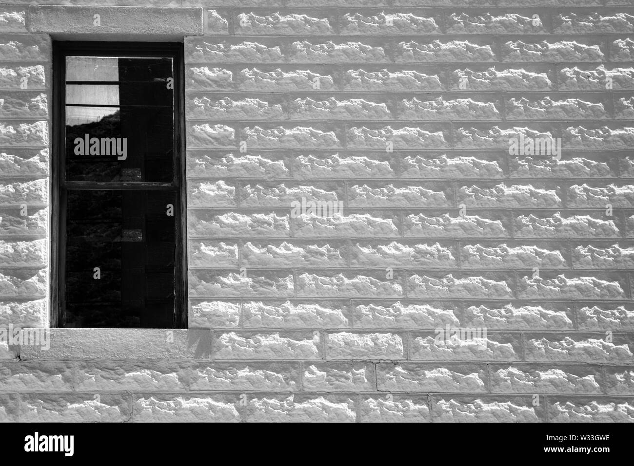 An old building made of Allen block, the texture off centers the lone dark window, in black and white, Southwest, USA, Stock Photo