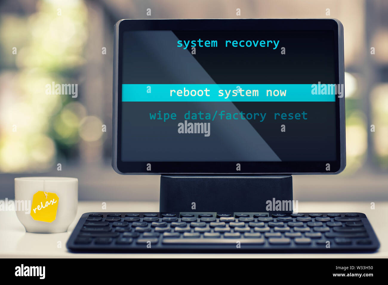 A tablet device with system recovery on the screen and about to be rebooted in a modern work setting with a tea cup that says relax. Stock Photo