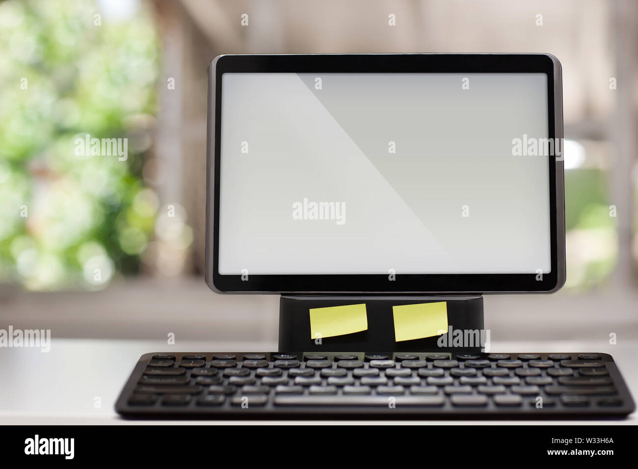 A computer with a touchscreen and wireless keyboard on a white desk with a window view in the background. Stock Photo