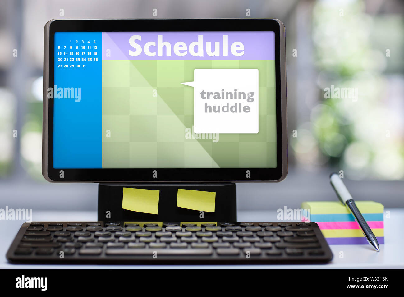A tablet computer workstation with mock up scheduling software application on a office desk with colorful sticky notes, a pen and wireless keyboard. Stock Photo