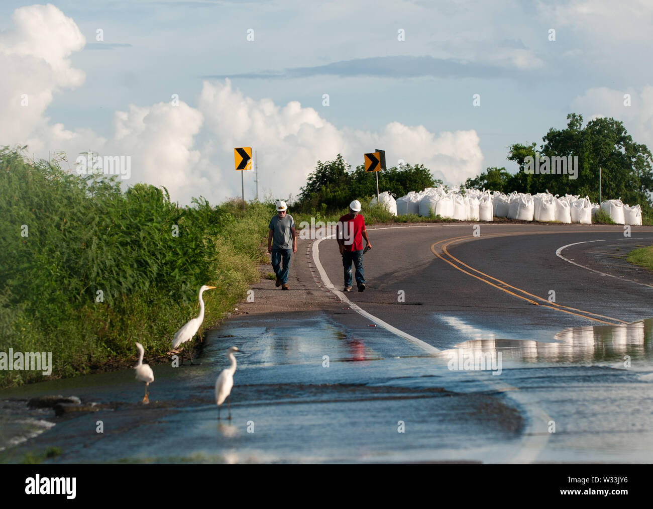 New Orleans, United States. 11th July, 2019. Men who work at an oil field south of Port Sulphur walk through a partially flooded road following flash floods and sporadic rains on Thursday. With the Mississippi River's water level at an all time high and a storm forming in the Gulf of Mexico that is expected to make landfall on the Louisiana and Texas coasts, many fear that levees will fail and that New Orleans will again be inundated as bad as it was in the 2004 aftermath of Hurricane Kartina. Credit: SOPA Images Limited/Alamy Live News Stock Photo