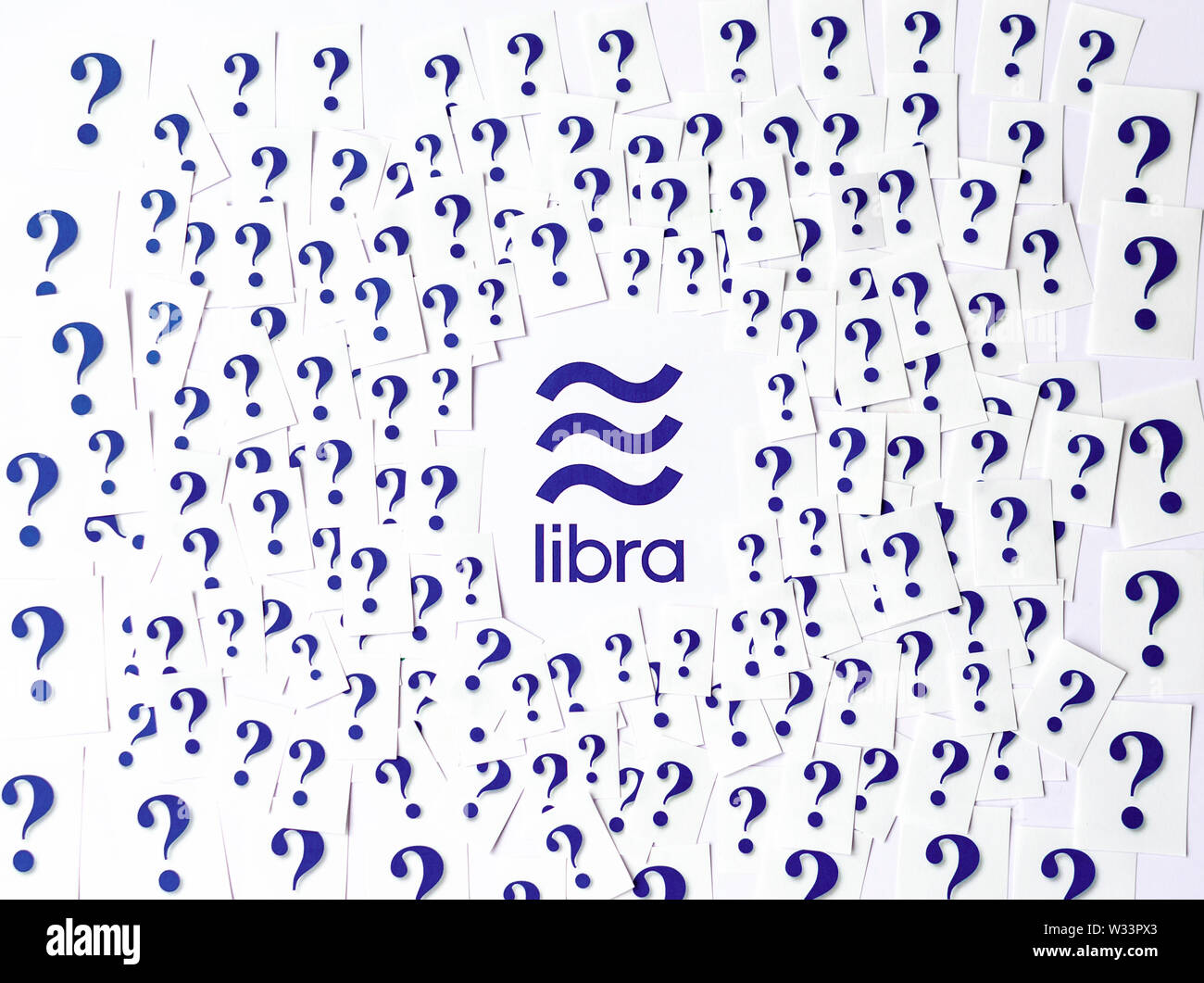 Facebook Libra logo printed with large number of cut paper question marks around. Conceptual photo: Libra raises questions and concerns around. Stock Photo