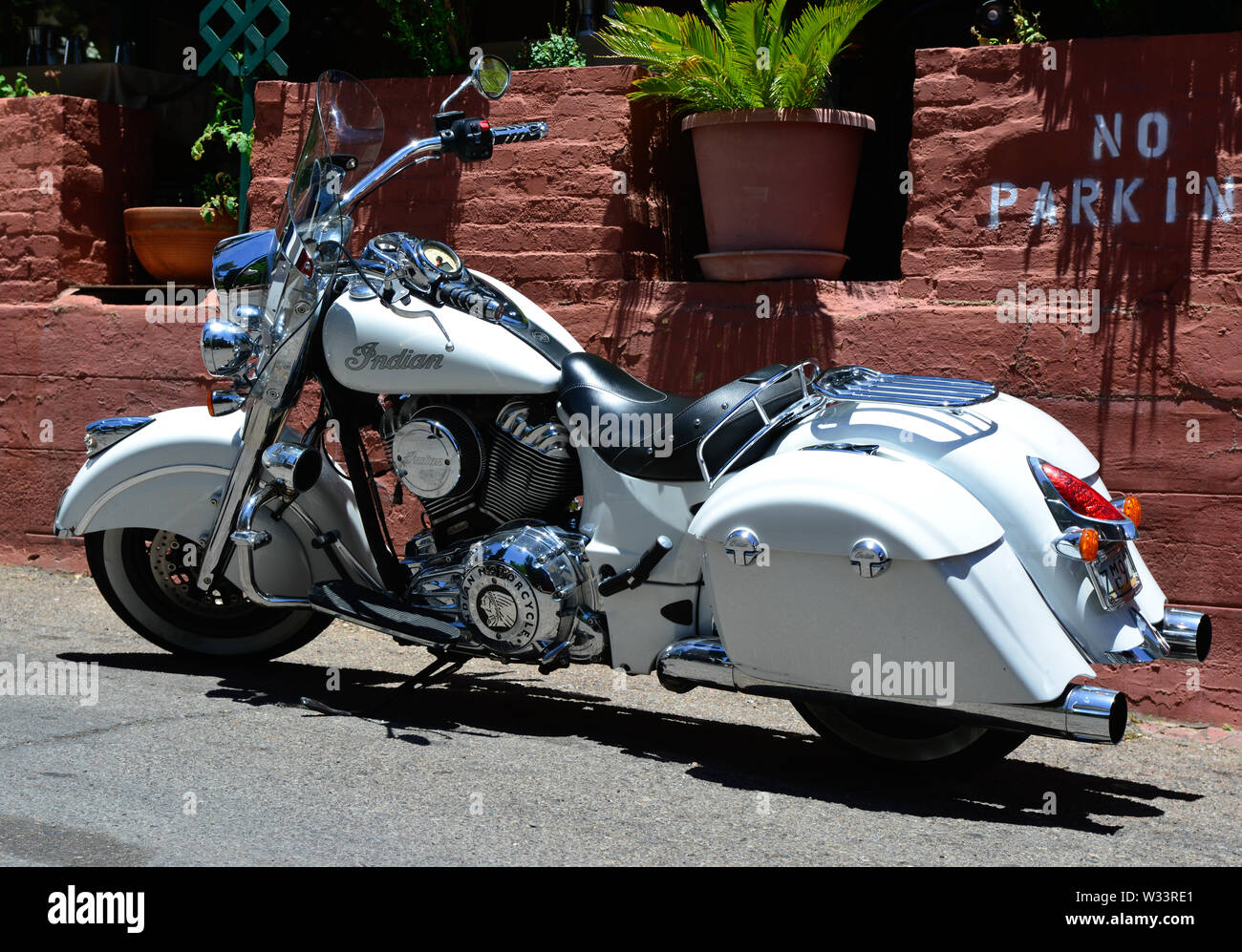 A beautiful white Indian motorcycle parked in a no parking zone near a brick wall with garden in the Southwestern USA, Stock Photo