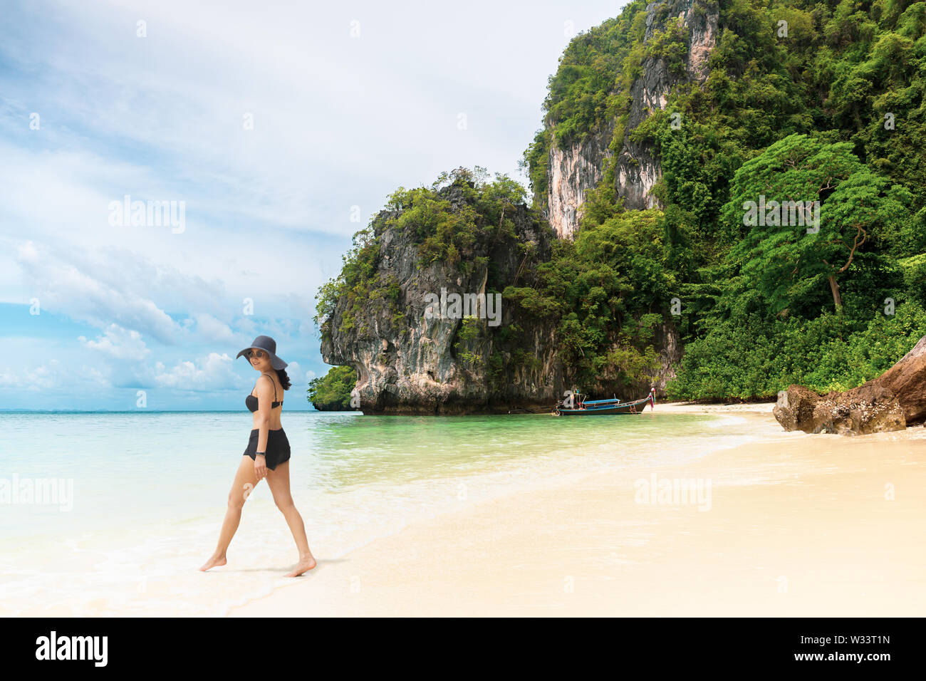 Happy smiling woman in bikini and sunhat walking on the beach Stock Photo