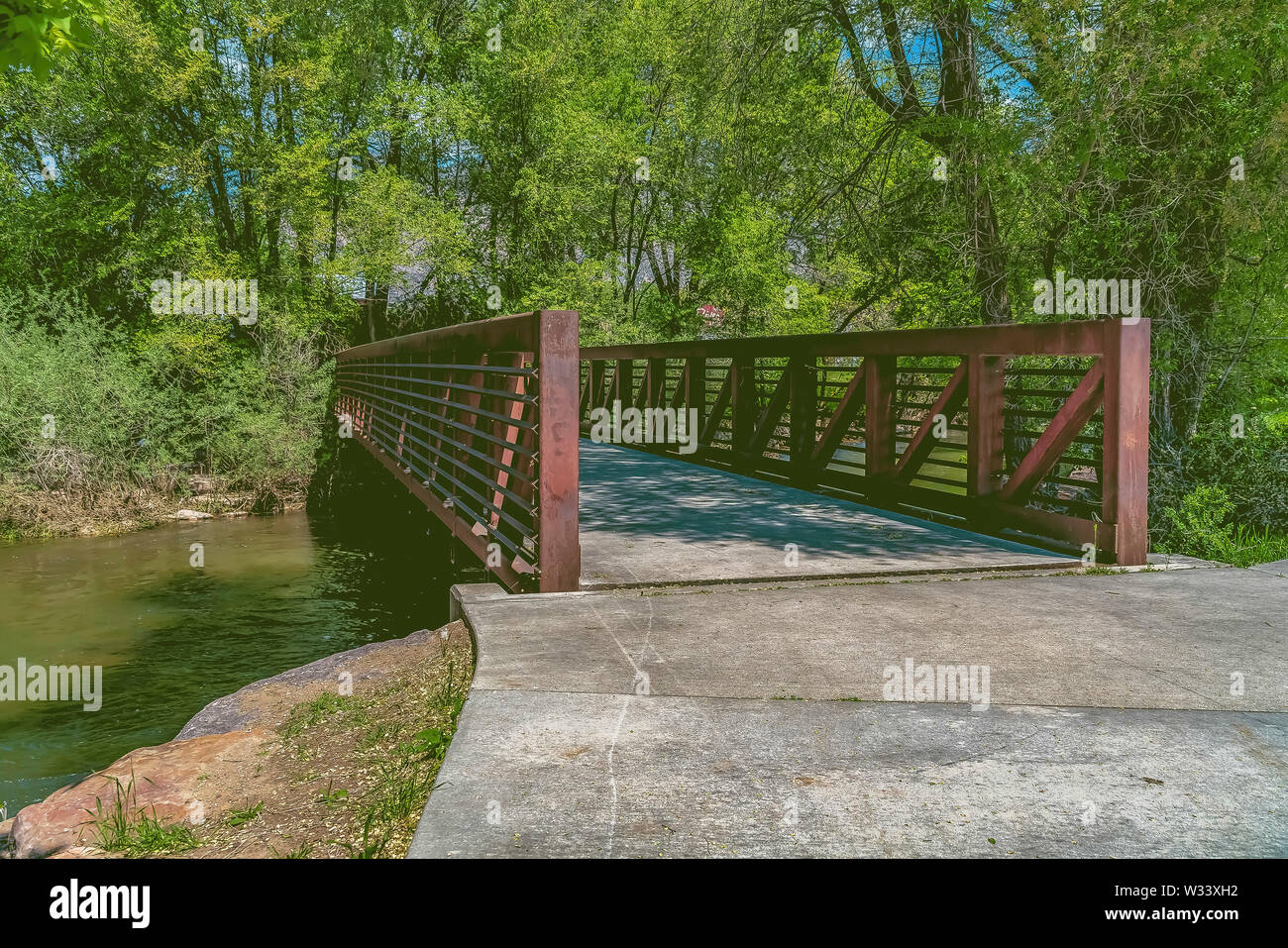 Bridge over a lake surrounded by lush trees against blue sky on a sunny ...
