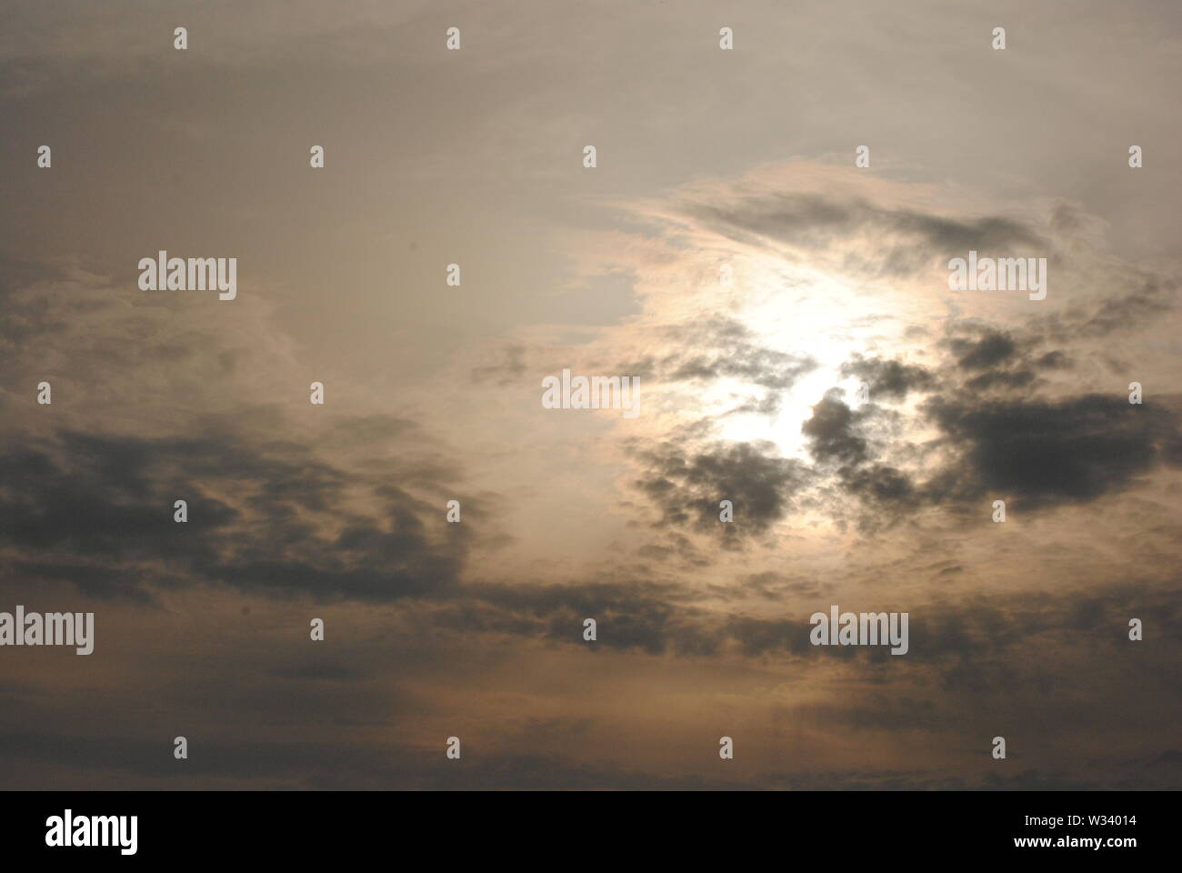 Hazy diffuse sun shining behind  grey clouds in a fuzzy  abstract sky Stock Photo