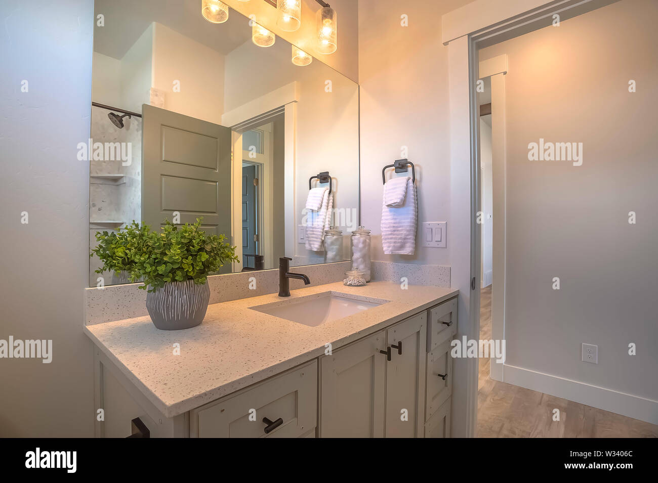 Mirror And Vanity Unit Inside A Bathroom With White Wall And Brown Wood Floor Wood Cabinets Are Beneath The White Countertop With A Single Basin Sink Stock Photo Alamy