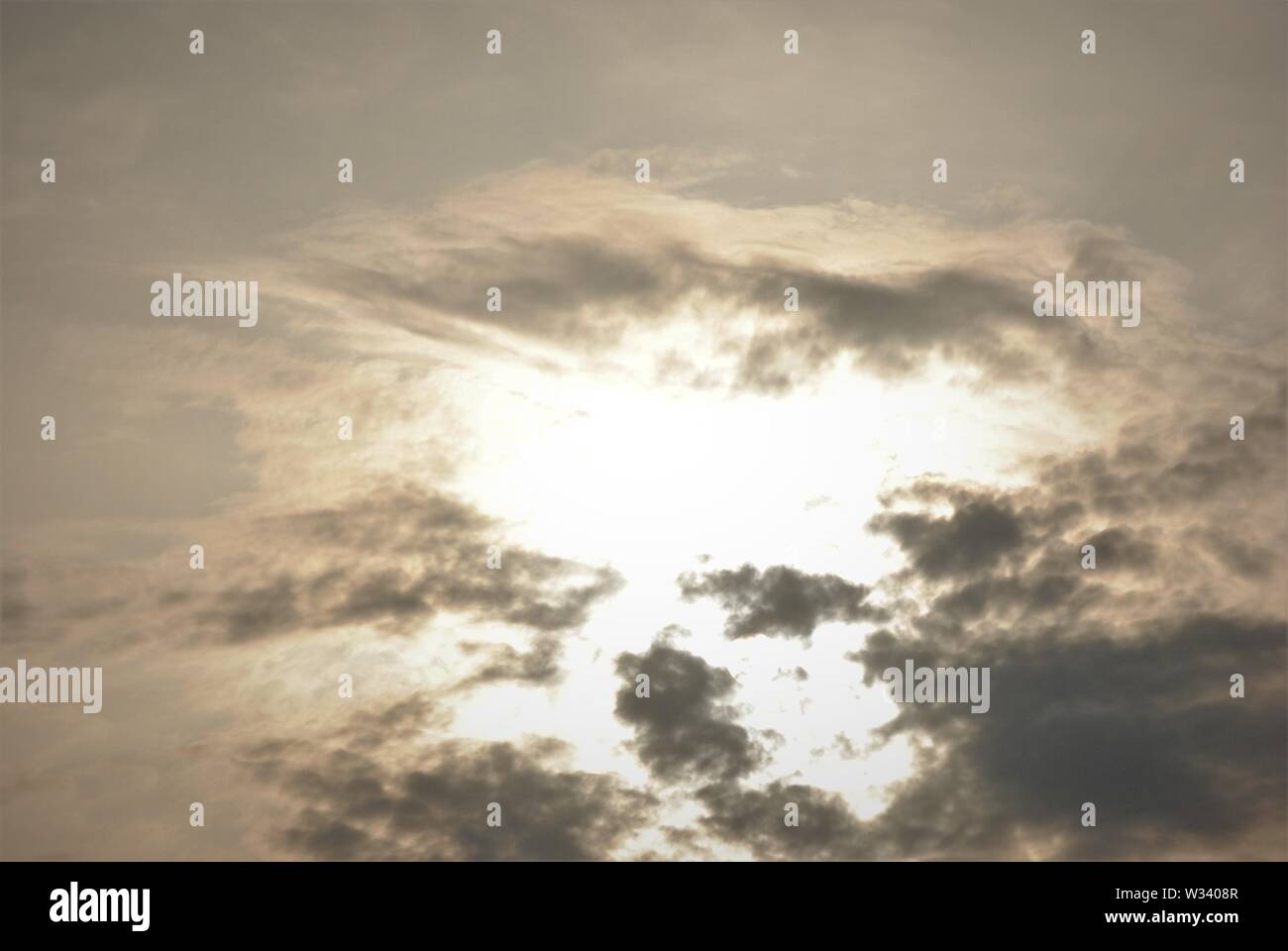 Hazy diffuse sun shining behind  grey clouds in a fuzzy  abstract sky Stock Photo