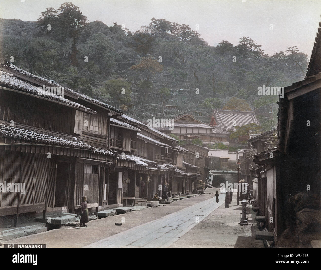 [ 1880s Japan - Japanese Street View at  Suwano-machi, Nagasaki ] —   Suwano-machi (諏訪町) in Nagasaki. The temple in the back is Koeizan Choshoji Temple (光栄山長照寺). Mt. Kazagashira (風頭山) is in the background. A lone water pump and gas lamp are on the right. Photographed between 1887 (Meiji 20) and 1892 (Meiji 25).  19th century vintage albumen photograph. Stock Photo