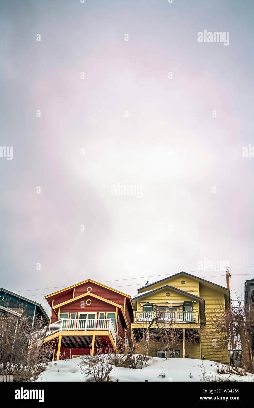 Vast cloudy sky over colorful houses and snow covered ground in winter. Porches, outdoor stairs, and balconies can be seen at the facade of the homes. Stock Photo