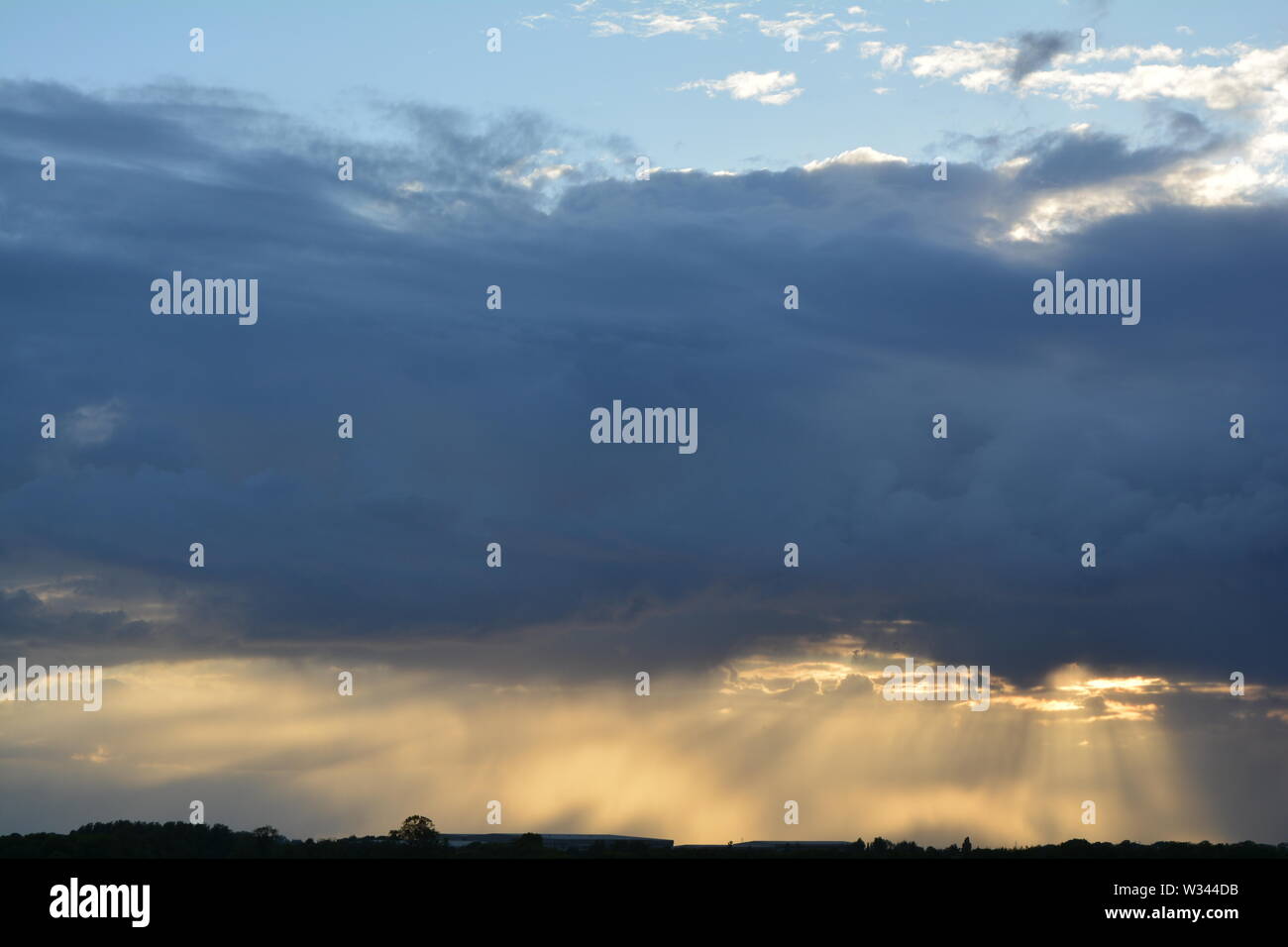 sun setting behind mixed clouds with rays of light showing below a ...