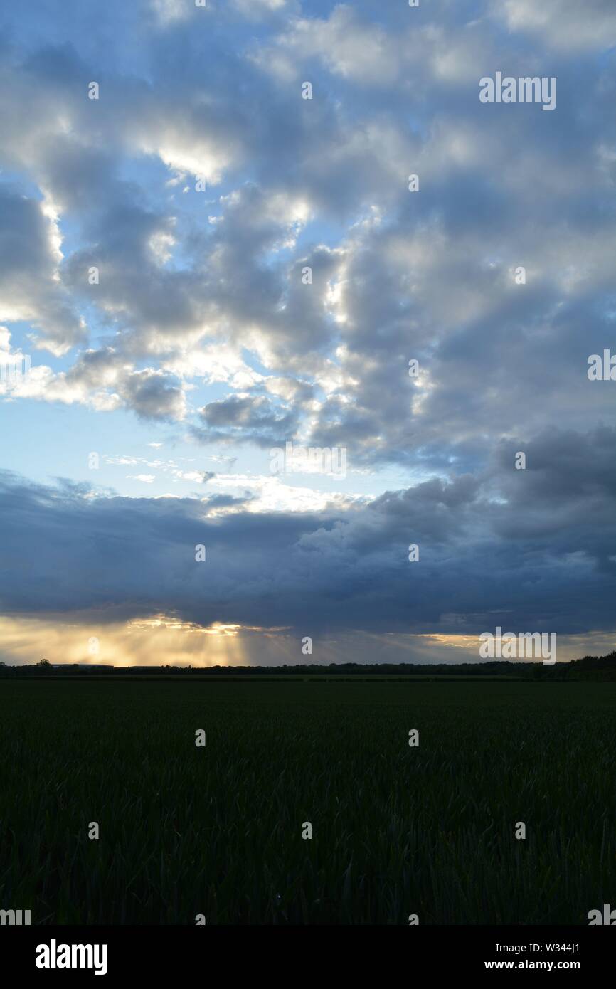 sun setting behind mixed clouds with rays of light showing below a ...