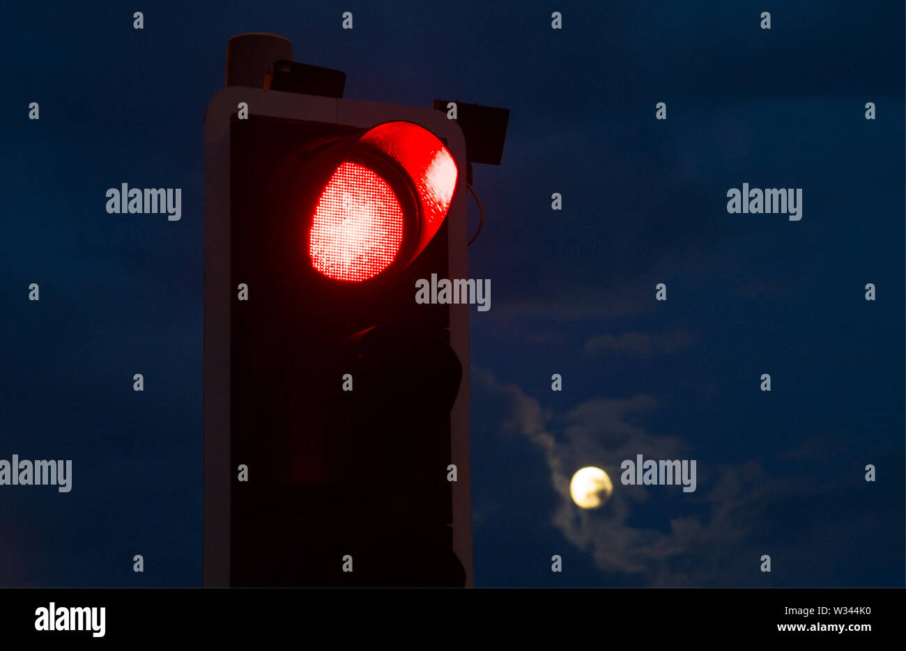 A red traffic light with a full moon in the background Stock Photo