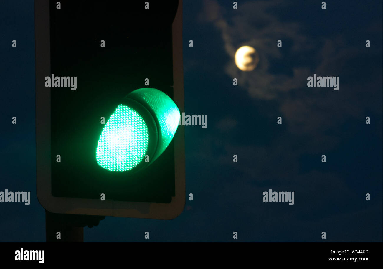 A green traffic light with a full moon in the background Stock Photo