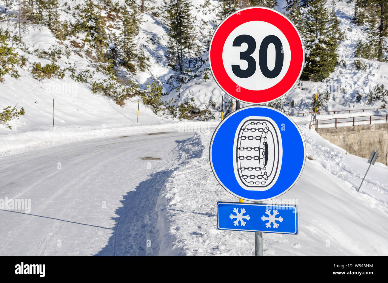 Snow chains mandatory road sign below a speed limit sign along a winding snowy mountain road Stock Photo