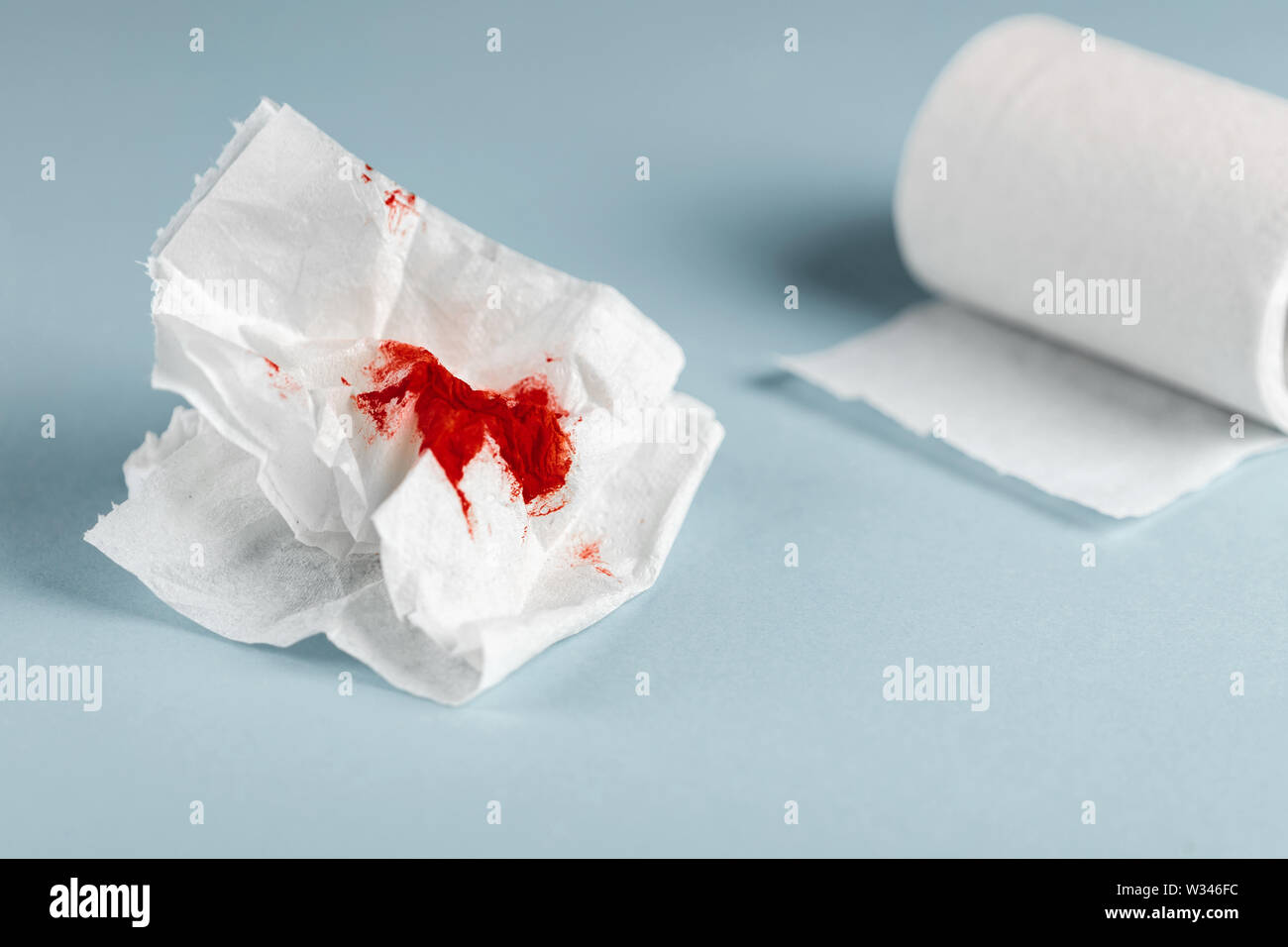 A photo of used bloody toilet paper and a toilet paper roll on the light blue background Stock Photo
