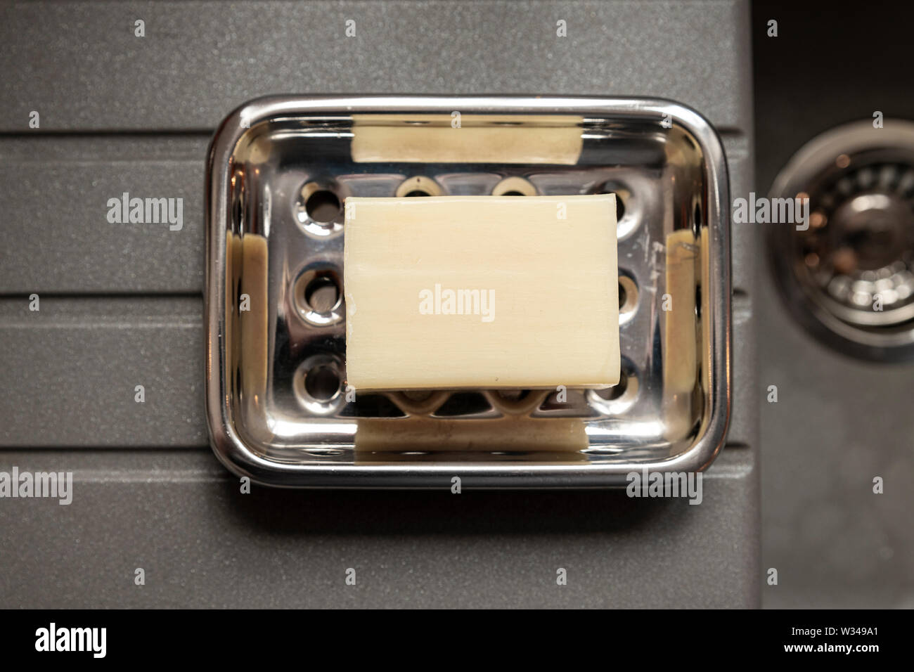 Bar of soap on a stainless steel dish on a grey kitchen granite like